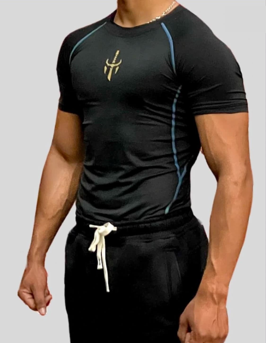 Gymcell black compression T-shirt with blue seam lines and a gold dagger mark on the chest.